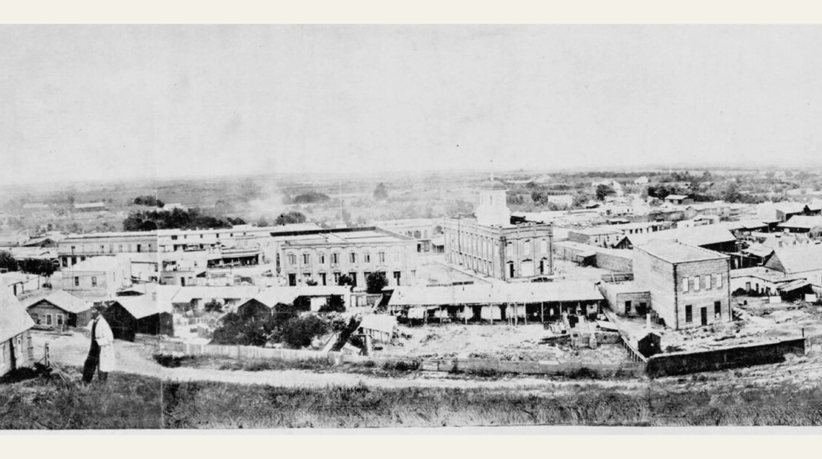 Black-and-white panoramic photograph of Los Angeles in 1869, showing low adobe and brick buildings and open land beyond